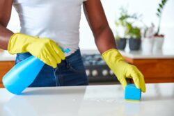 a close up image of a female wearing yellow house gloves wiping a counter with a spray bottle